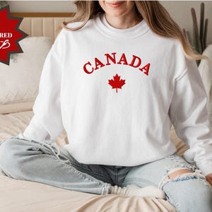 May include: White sweatshirt with red embroidered text "CANADA" and a red maple leaf.