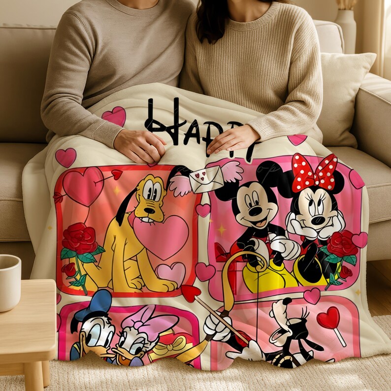 A couple is sitting on a couch, wrapped in a blanket featuring characters from Disney and Minnie Mouse.