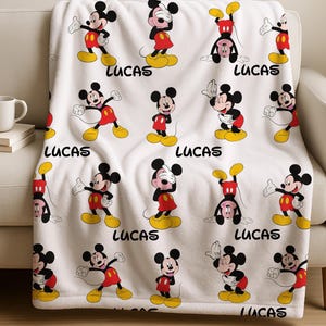 May include: White fleece blanket featuring a repeating pattern of Mickey Mouse in various poses. Mickey is wearing his signature red shorts, yellow shoes, and black gloves. The name "LUCAS" is printed in black below each Mickey Mouse image.