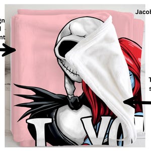 a pink blanket with a cartoon character design, including a skeleton and a red-haired character. The blanket is printed on the front, and the back is solid white.