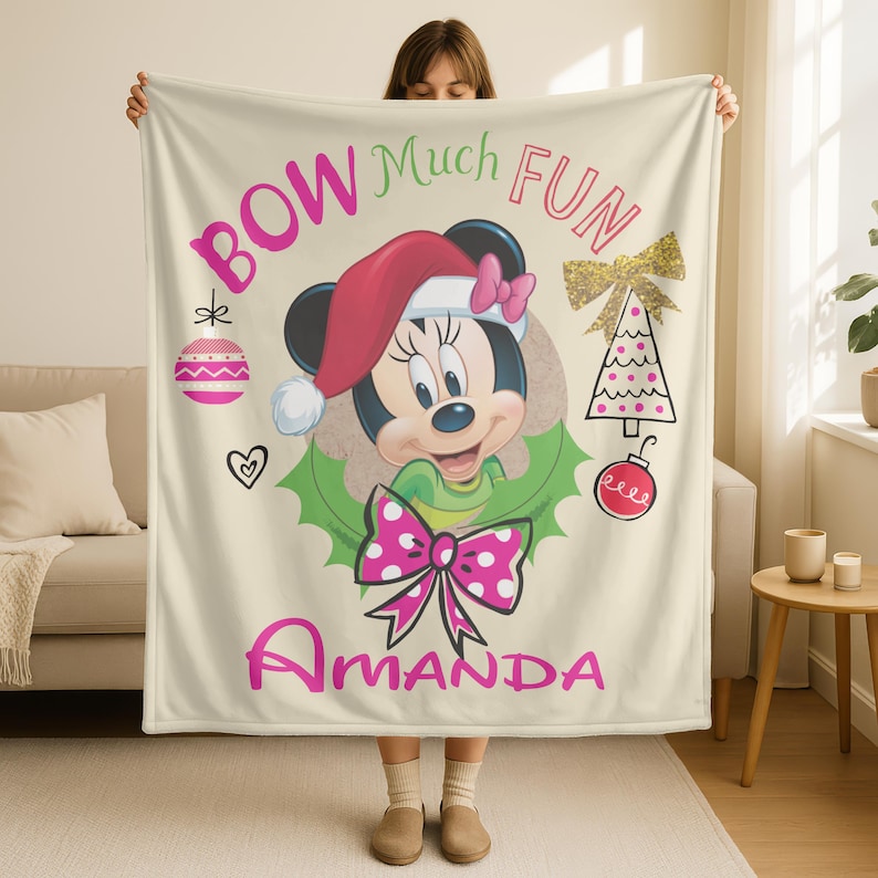 A woman is holding up a blanket featuring a Minnie Mouse character wearing a Santa hat and bow, with the text "BOW Much FUN Amanda" printed on it.