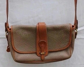 May include: A rectangular shoulder bag crafted from textured taupe leather with smooth tan leather trim. The bag features a central vertical strap closure with a metal buckle detail and an adjustable shoulder strap attached with gold-tone hardware.