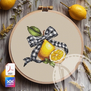 Pode incluir: Bordado em ponto cruz de um limão com um laço xadrez preto e branco, folhas verdes e metade de uma fatia de limão. O bordado está num bastidor de madeira. O fundo inclui limões e detalhes florais.