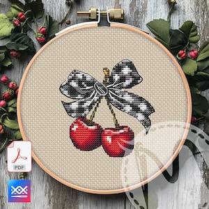May include: Cross-stitch embroidery of two red cherries with a black and white checkered bow. The embroidery is set in a wooden hoop, with a neutral-colored fabric background. The design is detailed and vibrant, showcasing a classic fruit motif.
