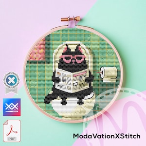 Puede incluir: Bordado de punto de cruz en un aro de madera que representa un gato negro con gafas rosas leyendo un periódico en el inodoro. El fondo es verde y rosa, con un rollo de papel higiénico en la pared. El texto "ModaVationXStitch" está en la parte inferior.