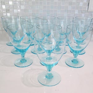 May include: A collection of clear, light blue stemmed glasses. The glasses have a rounded bowl and a circular base. The stem and base are the same light blue color as the bowl. The glasses are arranged in a group on a white surface.