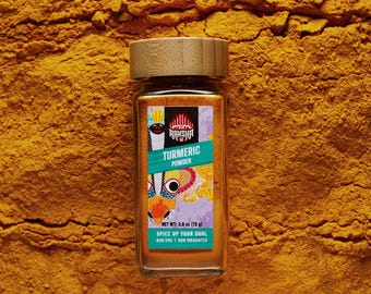May include: A glass jar of turmeric powder with a wooden lid, set against a backdrop of turmeric powder. The label reads "Raksha Turmeric Powder" and "Spice Up Your Soul." The jar contains 2.6 oz (75 g) of turmeric.