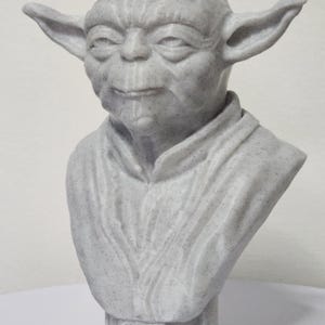 Puede incluir: Un busto blanco de Yoda de Star Wars, impreso en 3D. El busto está detallado con arrugas y una superficie texturizada.