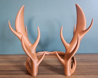 May include: A pair of brown, stylized antler headbands. The antlers are curved and have multiple points, with a smooth, matte finish. The headband is designed to be worn on the head for costume or cosplay purposes.
