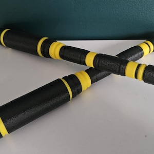 May include: Two black and yellow nunchucks are crossed against a teal background. The nunchucks have a textured black surface with yellow bands. The ends are rounded. The nunchucks are a martial arts training tool.