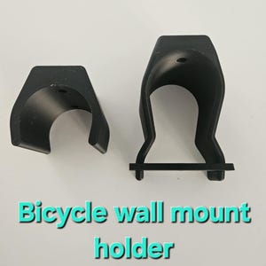 May include: Two black bicycle wall mount holders. These holders are made from a robust material and are designed to securely hold a bicycle against a wall. The text "Bicycle wall mount holder" is displayed in the image.