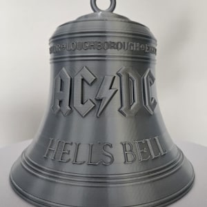 May include: A grey bell featuring the text "AC/DC" and "HELL'S BELLS". The bell has a loop at the top and is likely a decorative item or collectible. The word "LOUGHBOROUGH" is also visible.