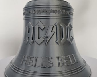 May include: A gray bell with the text "AC/DC" and "HELL'S BELL" in a stylized font. The bell has a loop at the top and is likely a decorative item or collectible.