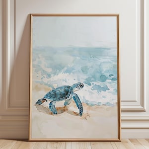 May include: Watercolor print of a sea turtle on a sandy beach with ocean waves in the background. The turtle is blue and the artwork is framed in a light wood frame. The artwork is displayed on a white wall.