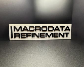 May include: White rectangular sign with black text that reads "MACRODATA REFINEMENT".