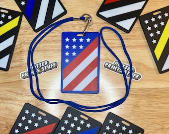May include: A collection of rectangular ID badge holders with various flag designs, including the American flag, a red stripe, a blue stripe, and a yellow stripe. A blue lanyard is attached to the American flag badge. The text "POTTER PRINTS STUFF" is visible.