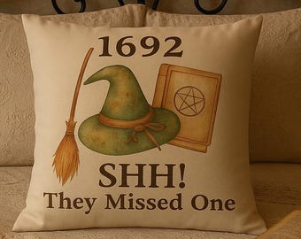 May include: A cream-colored decorative pillow with a witch-themed design. The pillow features a green witch hat, a broom, and a book with a pentagram. The text on the pillow reads "1692 SHH! They Missed One."