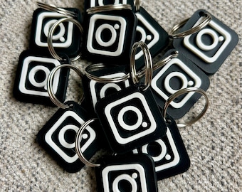 May include: A group of black and white Instagram logo keychains with silver key rings. The keychains are made of a smooth, plastic-like material.