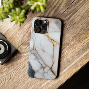 May include: A white and gold marble phone case with a camera lens cutout. The case has a white background with gold veins running through it.