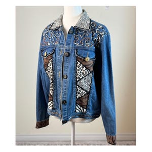 Peut inclure: Veste en jean bleue avec un design patchwork unique. La veste présente des panneaux à imprimé animalier marron, noir et blanc, ainsi que des détails brodés sur le col et la poitrine. Elle possède des boutons et des boutons décoratifs.
