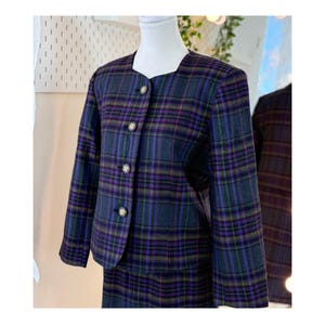 May include: A vintage two-piece suit with a plaid design. The jacket has a rounded neckline, long sleeves, and gold buttons. The plaid pattern includes blue, purple, green, and pink hues. The skirt is visible at the bottom of the image.