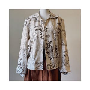 Può includere: Una giacca color crema con stampa floreale marrone. La giacca ha una chiusura con bottoni sul davanti e maniche lunghe.