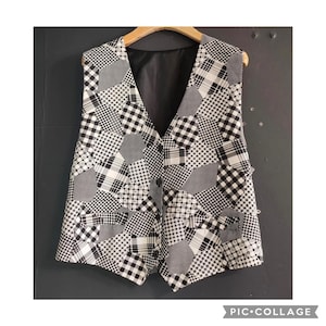 May include: A black and white patchwork vest with a V-neck and button closure. The pattern is made up of various geometric shapes. The vest is hanging on a wooden hanger. The interior lining is black.