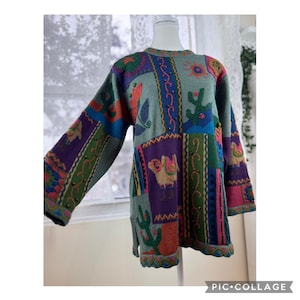 May include: A long-sleeved sweater with a patchwork design featuring cacti, suns, and other Southwestern-inspired motifs. The sweater has a mix of colours, including green, purple, blue, and orange. The sweater is displayed on a mannequin.