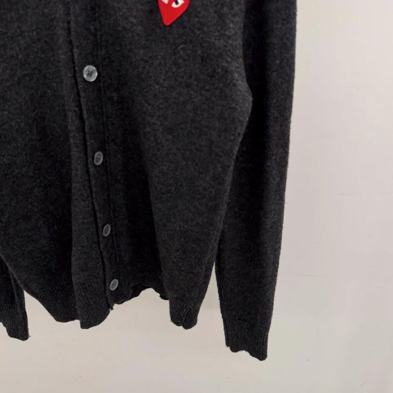 May include: Dark gray cardigan sweater with a red heart logo on the upper left chest. The sweater has a button-up front and long sleeves. The fabric appears to be a soft knit.