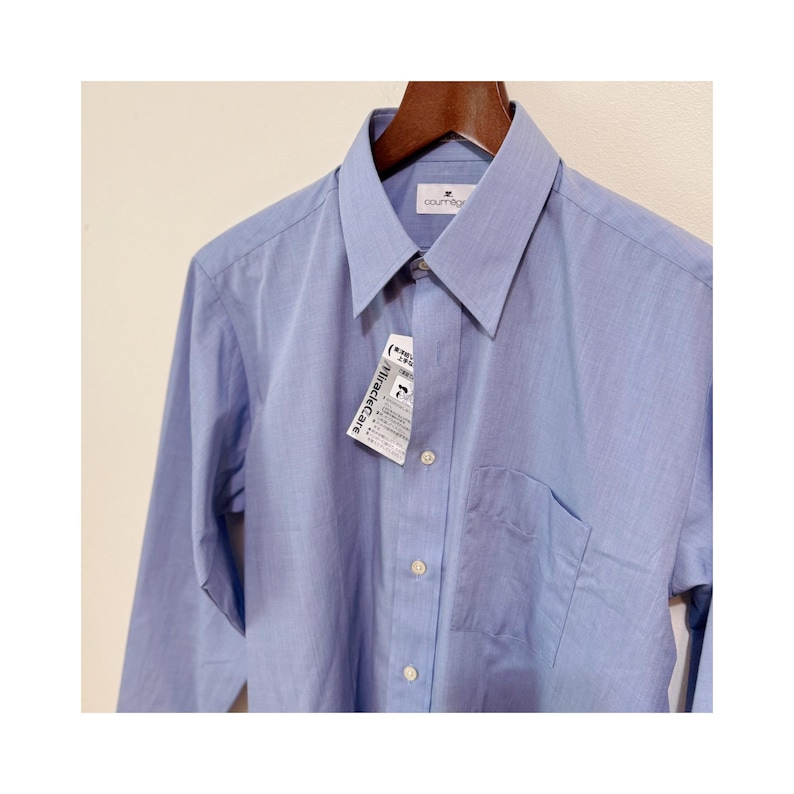 Puede incluir: Una camisa azul claro con botones, bolsillo en el pecho y mangas largas. La camisa est&aacute; colgada en una percha de madera. Una etiqueta con el texto "MiracleCare" est&aacute; adjunta.