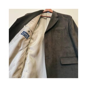 Op de afbeelding: Een bruine suède blazer met een enkele knoopsluiting en een zak aan de linkerkant. De blazer heeft een beige voering met een "CHAPS Ralph Lauren" label.