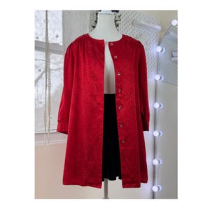 Puede incluir: Una chaqueta roja brillante, de manga larga, con un estampado floral y cierre de botones. La chaqueta se exhibe en un maniquí, combinada con una falda negra y una blusa blanca. La chaqueta tiene cuello redondo.