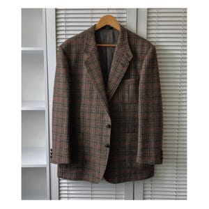 May include: A brown and red plaid blazer with a two-button closure and a notched lapel. The blazer is hanging on a wooden hanger against a white background.
