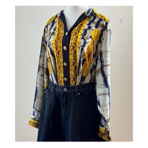 Może przedstawiać: Koszula z długim rękawem we wzór z żółtymi, granatowymi i beżowymi pionowymi paskami oraz złotymi akcentami. Koszula jest połączona z dżinsami z ciemnego denimu. Koszula ma klasyczny kołnierzyk i złote guziki.