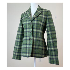 Puede incluir: Blazer verde a cuadros con un diseño clásico y a medida. La chaqueta presenta un cierre de tres botones y solapas con muescas. El estampado a cuadros incluye tonos de verde, azul marino y crema. El blazer se muestra en un maniquí.