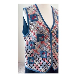 May include: A quilted vest with a woven pattern in red, white, blue, and grey. The vest has a denim trim and small square patches with floral embroidery. It features a V-neck and button closure.