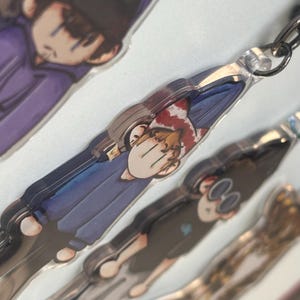 May include: Multiple clear acrylic keychains with cartoon character designs. Each keychain has a silver chain and clasp. The characters are dressed in different outfits and poses, with a range of colours used in the designs.