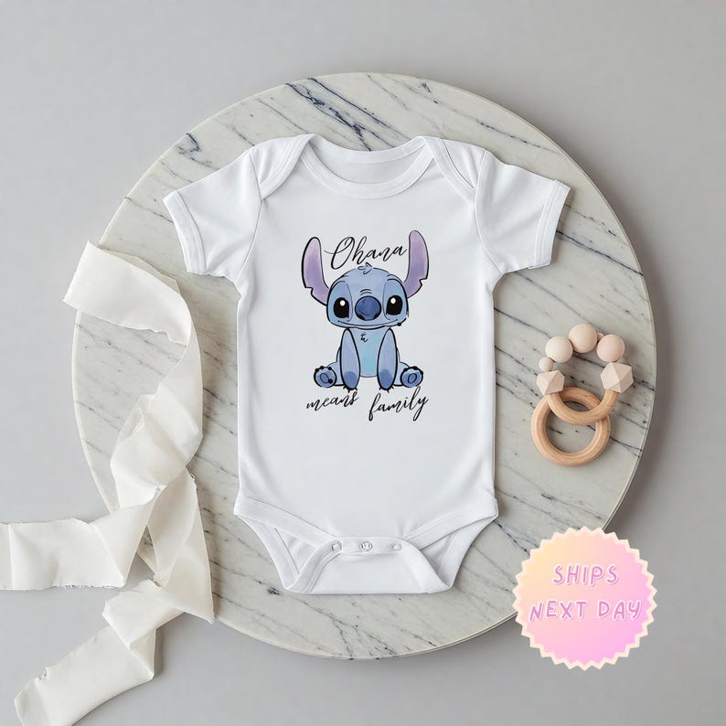 Op de afbeelding: Witte baby romper met een blauw Stitch-personage uit Lilo & Stitch. De romper heeft de tekst "Ohana means family".