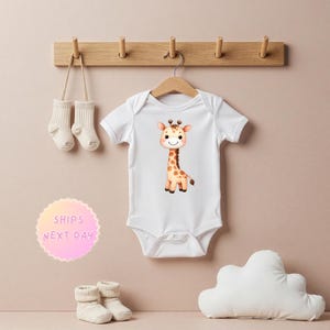 May include: White baby onesie with a cartoon giraffe illustration. The giraffe is brown with orange spots and has a friendly expression.