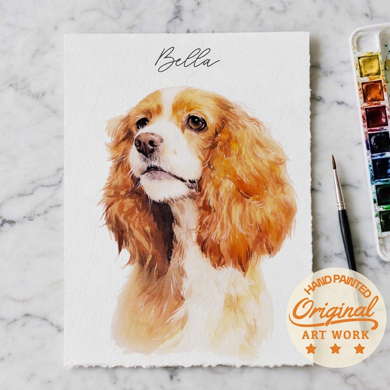 Puede incluir: Pintura a la acuarela de un perro Cocker Spaniel con pelaje marr&oacute;n y blanco. El nombre del perro, "Bella", est&aacute; escrito encima del retrato. La obra de arte est&aacute; etiquetada como "Hand Painted Original Art Work".