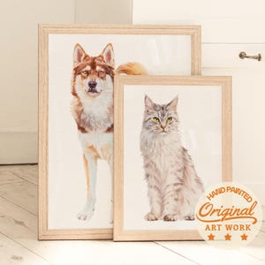 Puede incluir: Dos pinturas en acuarela enmarcadas de animales. Una representa un perro marr&oacute;n y blanco, la otra un gato gris con ojos amarillos. Ambas est&aacute;n en marcos de madera clara. Una pegatina en la parte inferior derecha dice "Hand Painted Original Art Work."