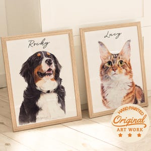 Puede incluir: Dos retratos en acuarela enmarcados de mascotas. Uno presenta un perro de monta&ntilde;a bern&eacute;s llamado Rocky, el otro un gato llamado Lucy. Ambos est&aacute;n en marcos de madera clara. La obra de arte est&aacute; etiquetada como "Hand Painted Original Art Work."