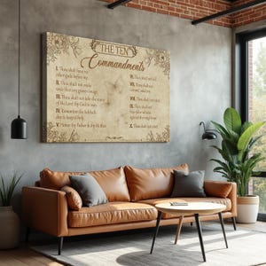 May include: A framed canvas print of "The Ten Commandments" in a neutral color palette. The text is displayed in a classic font, with floral and butterfly accents. The artwork hangs above a brown leather sofa in a modern living room setting.
