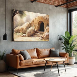 May include: A large canvas art print depicting a stone archway entrance to a cave, with steps leading up. The artwork is displayed above a brown leather sofa with gray pillows. A round wooden coffee table and a potted plant are in front of the sofa.