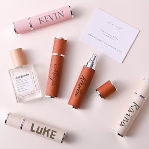 Puede incluir: Vista aérea de frascos de perfume y pulverizadores de viaje personalizados. Los pulverizadores son de color rosa, marrón y crema, con nombres como "Kevin", "Mirza" y "Kirsten". También hay un frasco de perfume transparente con tapón de madera.