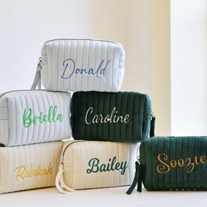 May include: Six quilted cosmetic bags in shades of blue, cream, and green, each embroidered with a name. The bags have zip closures and small handles. Measurements are in centimeters.