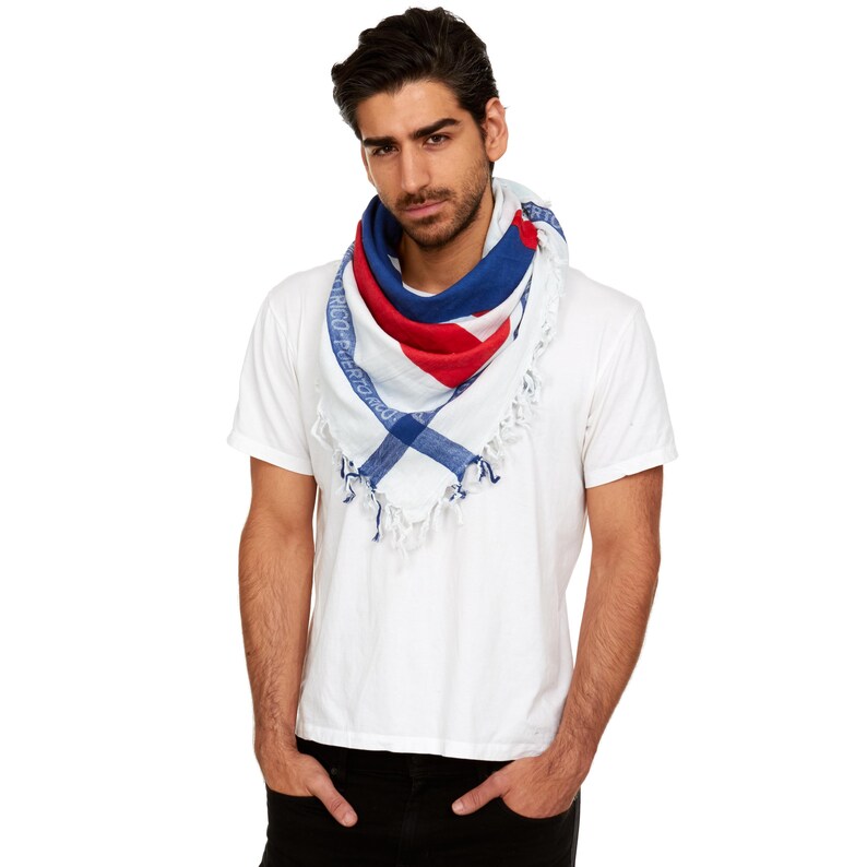 May include: A white short-sleeved t-shirt paired with a triangular scarf featuring a red, white, and blue pattern. The scarf has a blue border with the text Puerto Rico printed in white, and the edges are finished with white knotted fringe.