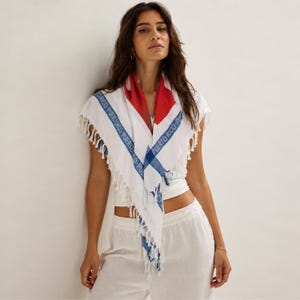 May include: A white triangular scarf featuring a red section at the top and blue stripes along the edges. The blue stripes contain the repeated text PUERTO RICO in a sans-serif font. The scarf has a fringe trim along the bottom edges.
