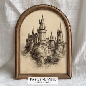 A vintage sketch of a wizarding school castle is elegantly framed in gold, offering a touch of wizard room decor. This enchanting wizard school art piece sets a moody, literary aesthetic against a cream wall.