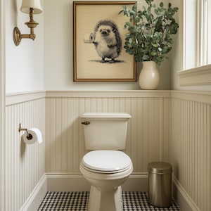 A whimsical hedgehog print with funny bathroom wall art humor is elegantly framed above a classic toilet, complemented by vintage lighting and a chic vase with greenery.